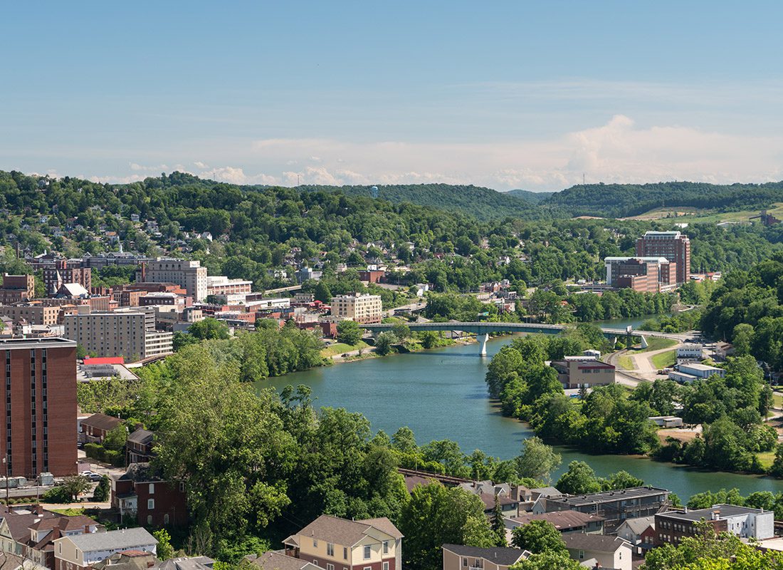 Morgantown, WV - Aerial View of Morgantown WV Displaying Buildings, Trees, and a Bridge Crossing Over a River on a Sunny Day